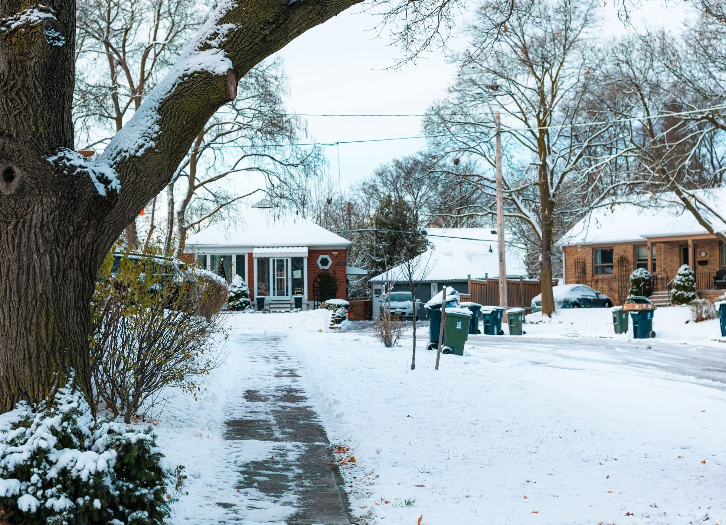 Snowy residential street of brick bungalows with bins at the curb