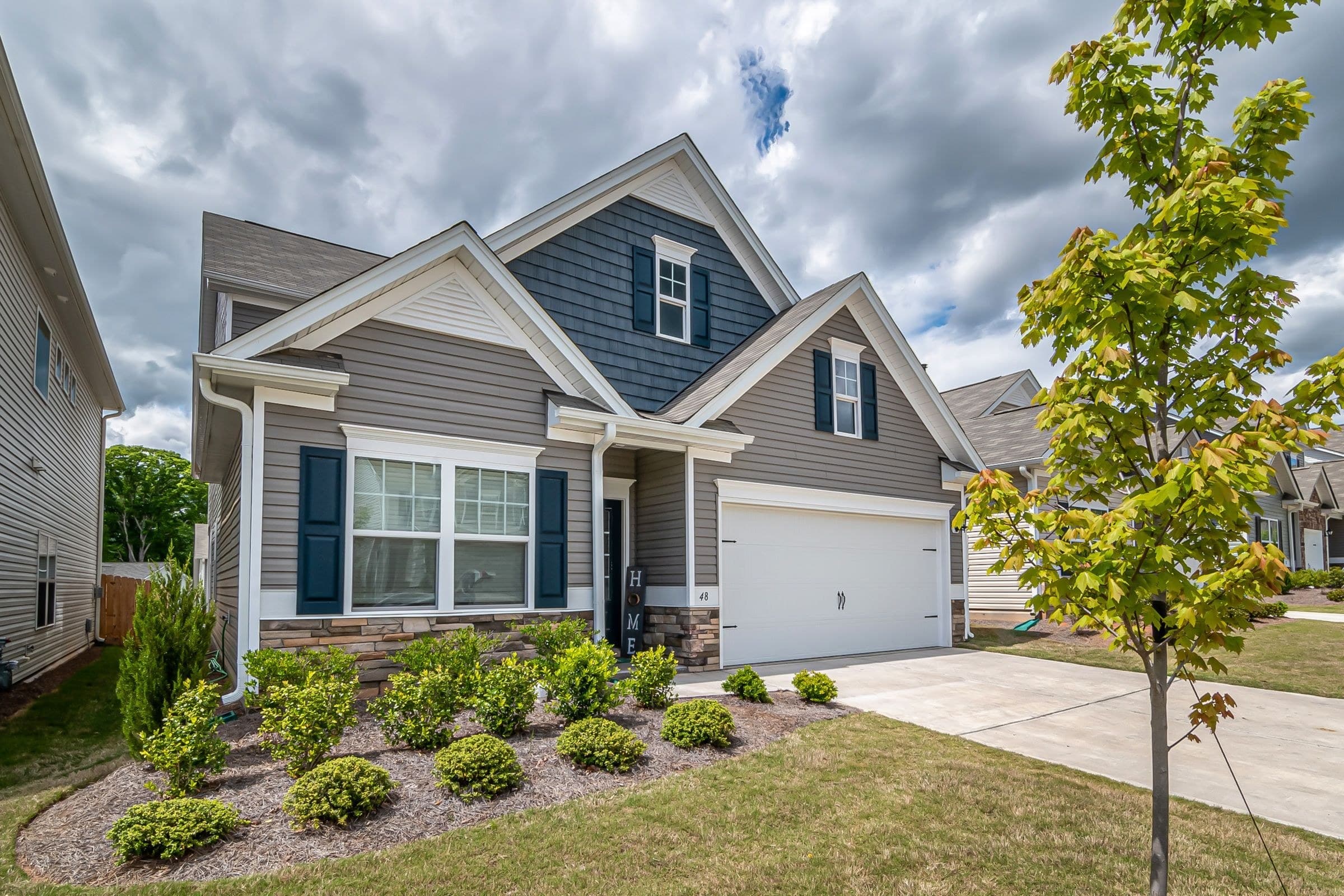Grey two-storey house with navy shutters and a double garage on a new suburban street