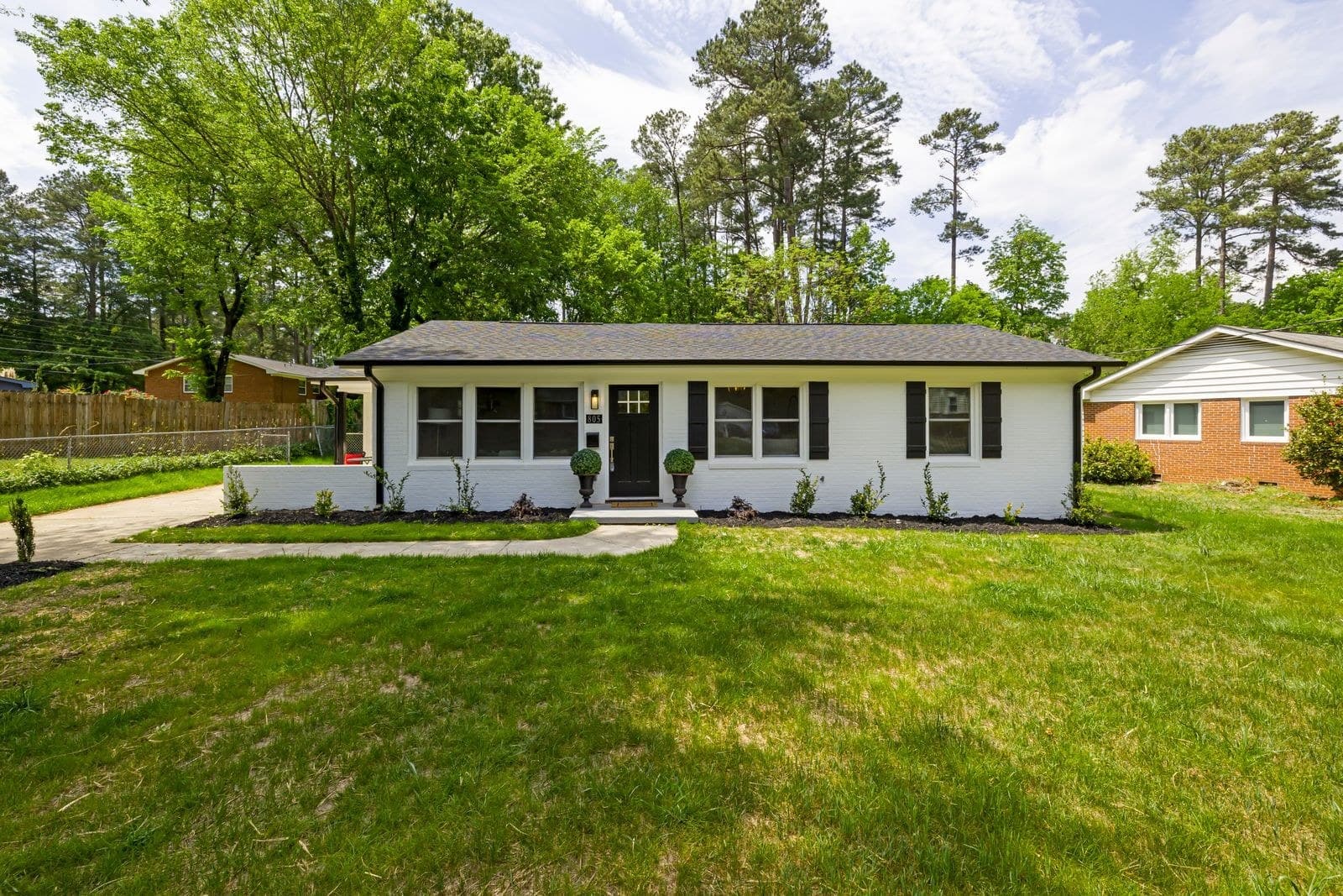White painted brick bungalow with black shutters and a wide front lawn