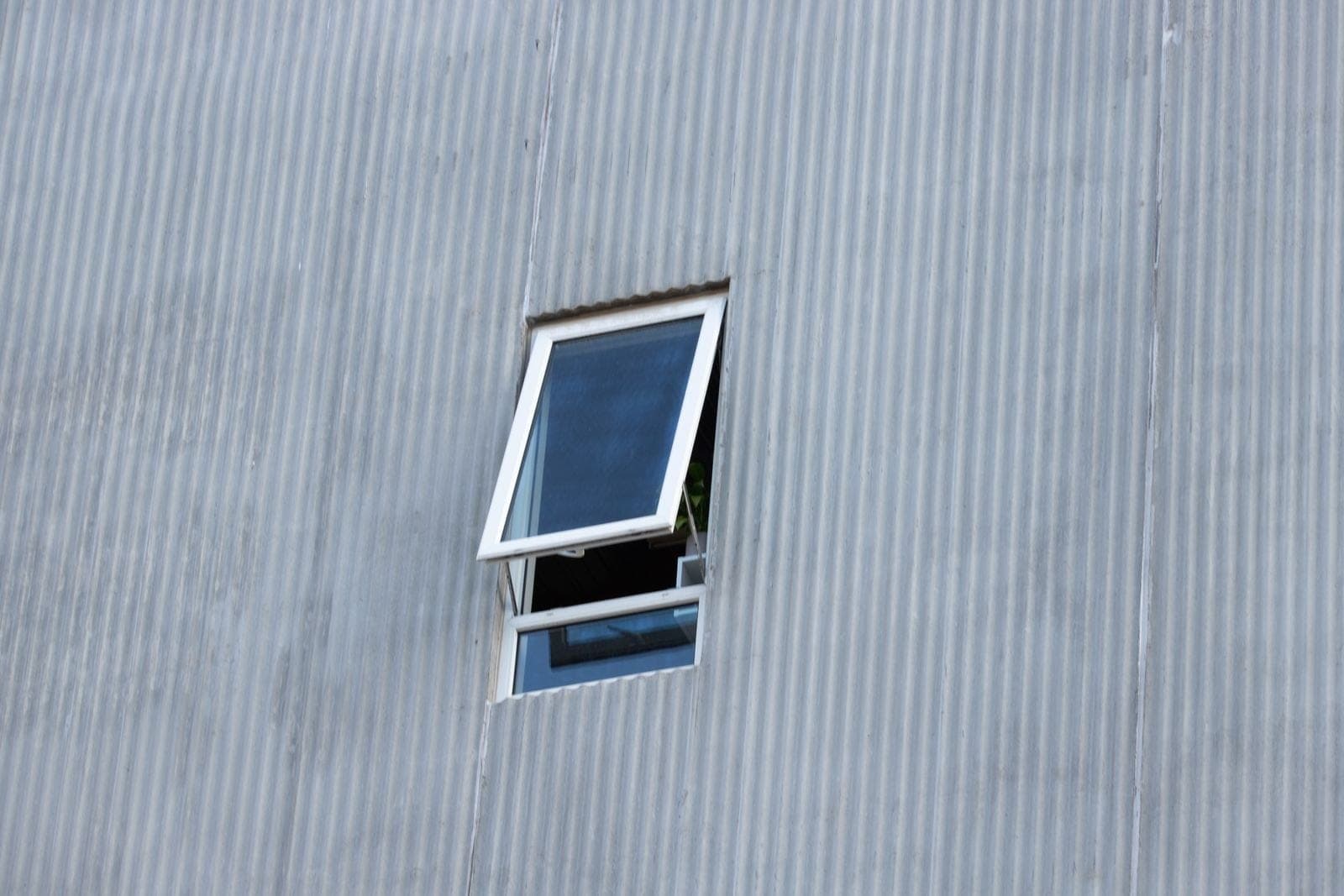 White awning window tilted open at the bottom in a grey wall