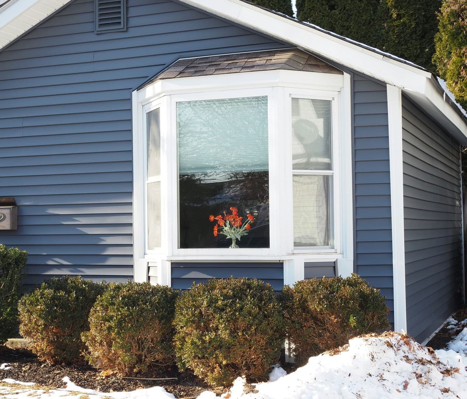 Blue sided house with a white bay window and snow on the ground