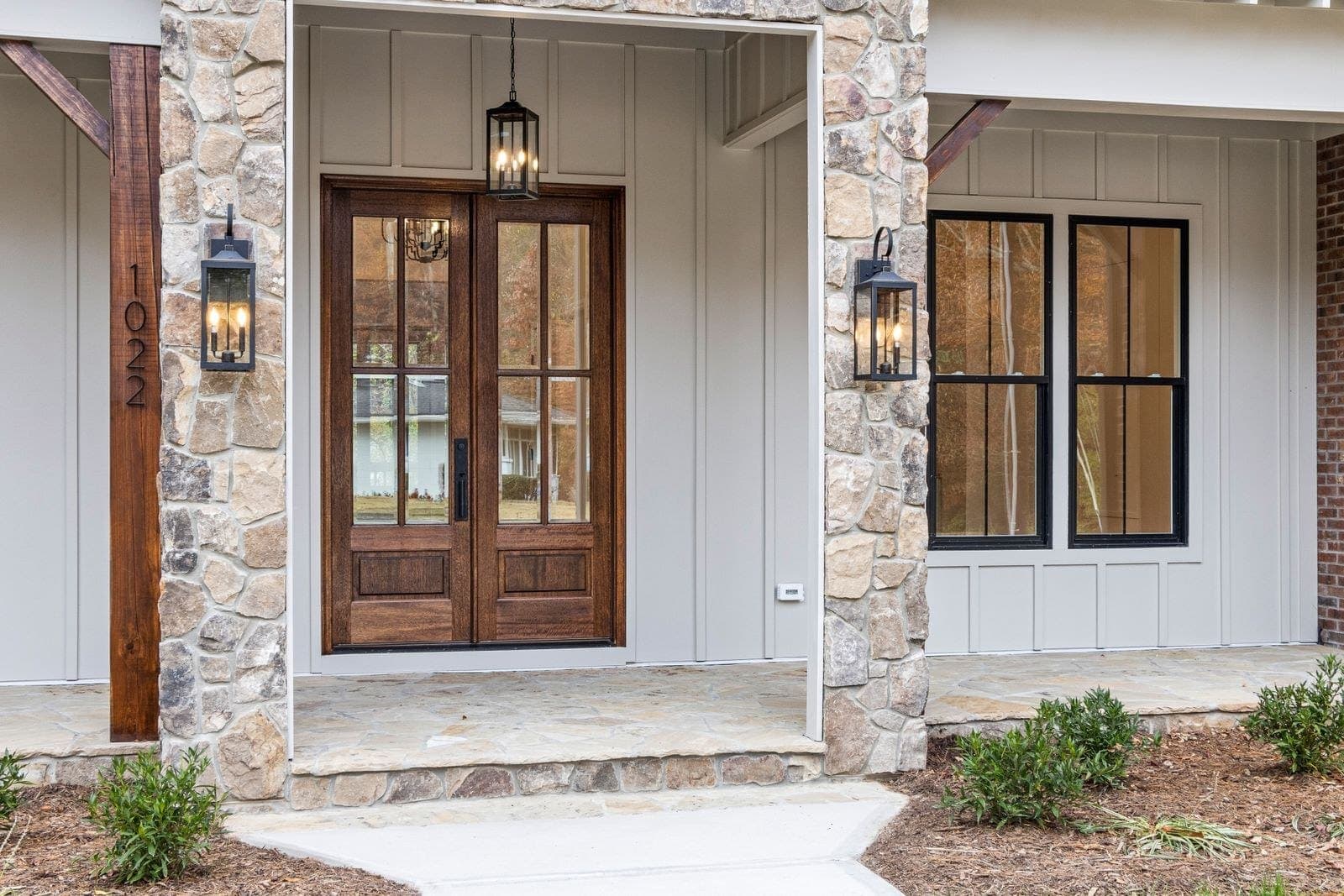 Wood-look double entry doors between stone pillars with lantern lights
