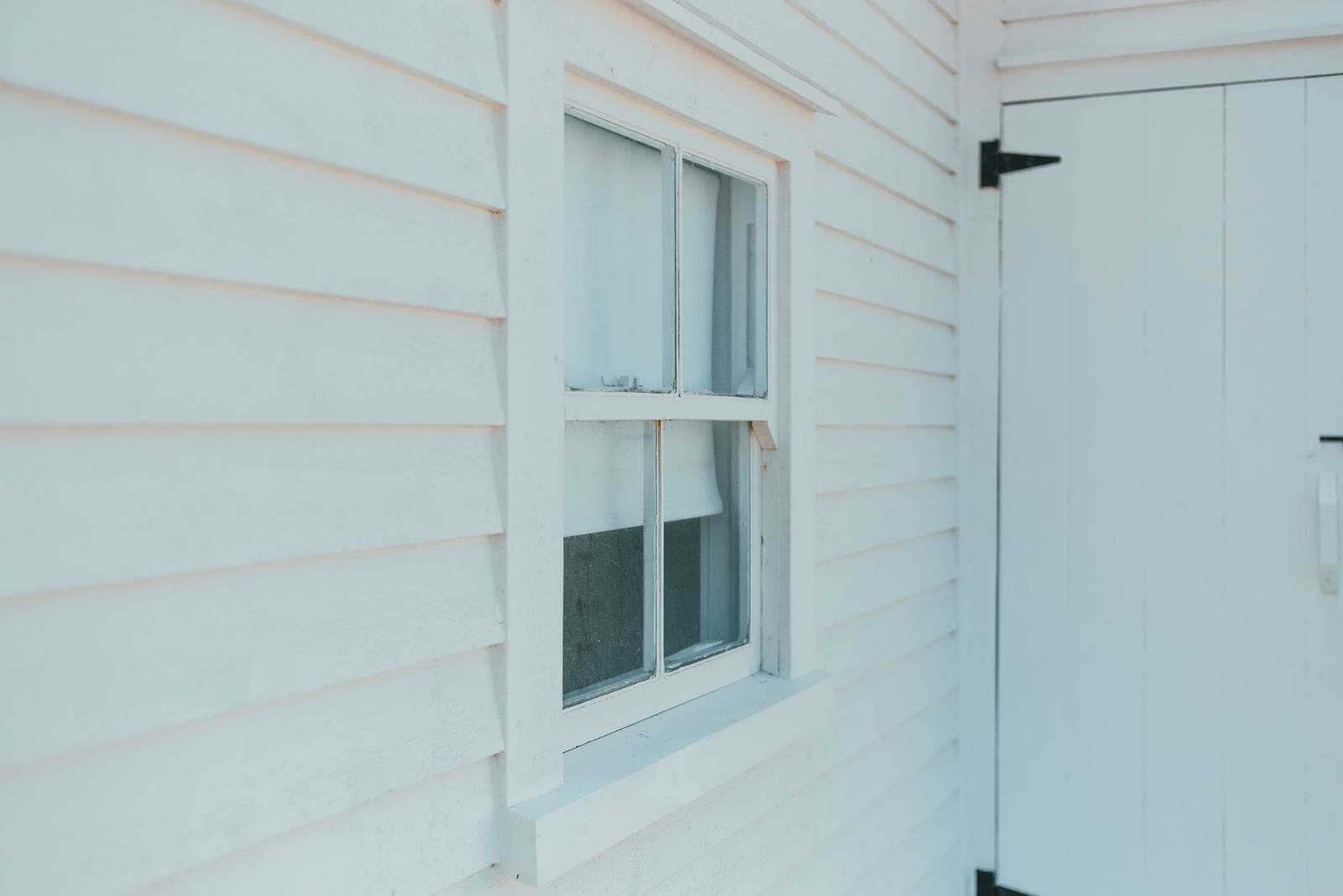 White hung window in white wood siding beside a door
