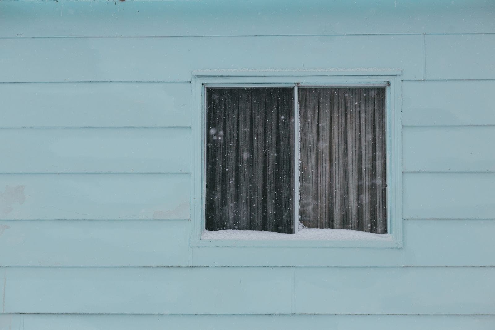Two-pane sliding window in pale blue siding with snow on the sill