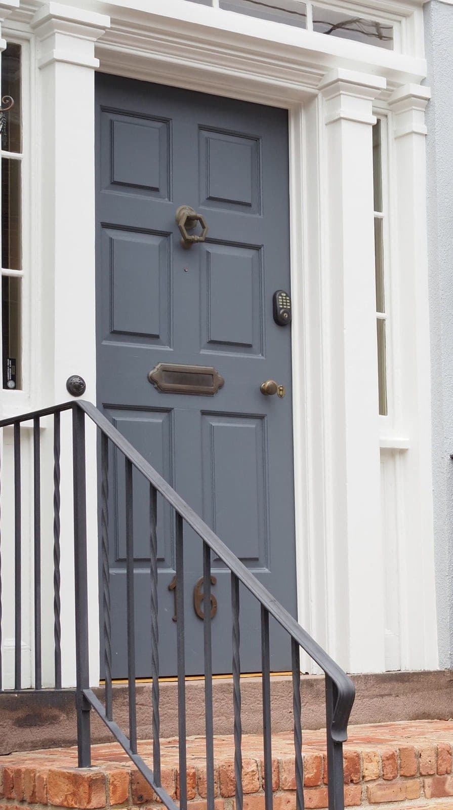 Painted grey front door beside shuttered windows above brick steps