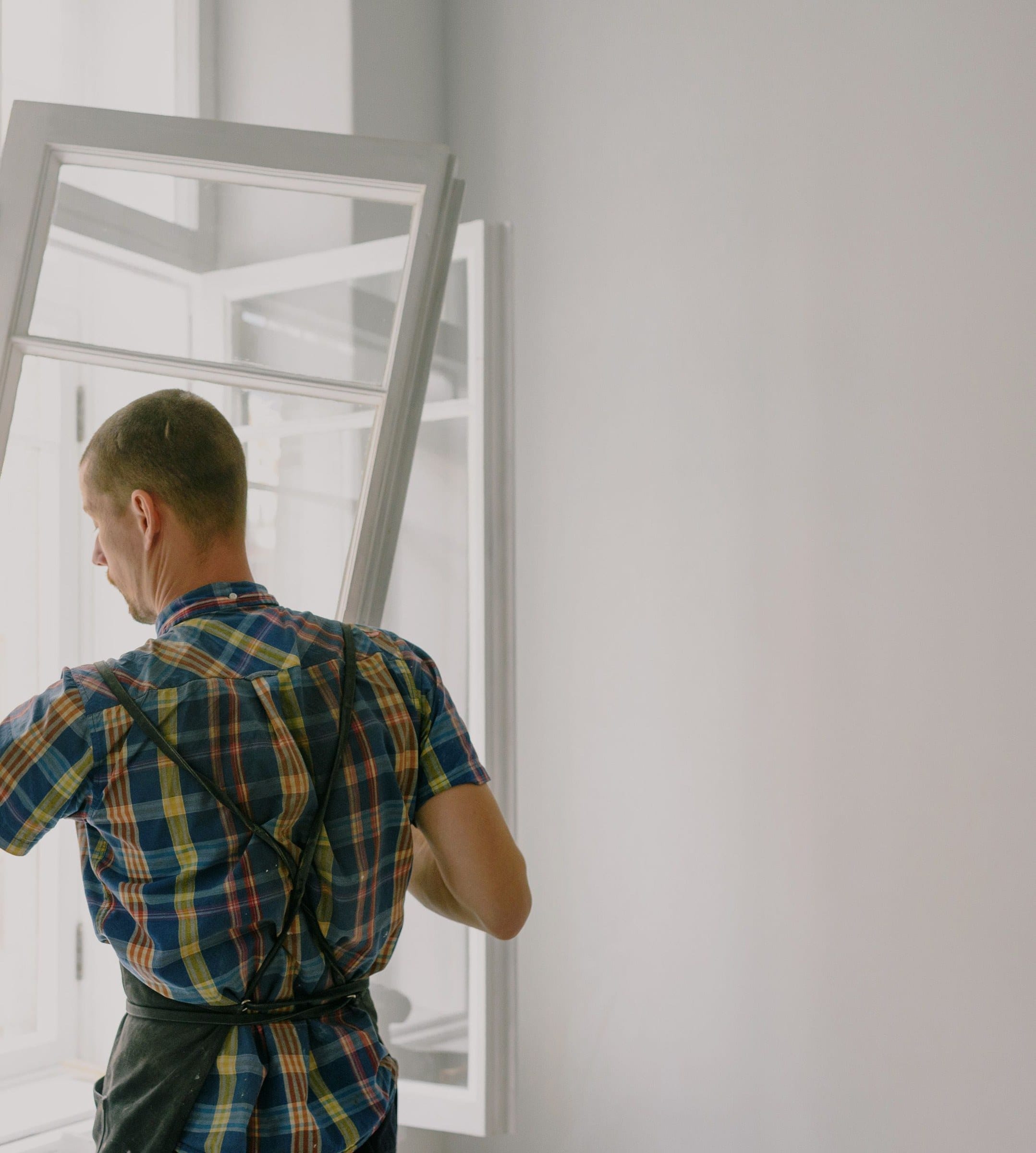 Installer lifting a new white window frame into an opening during a window replacement